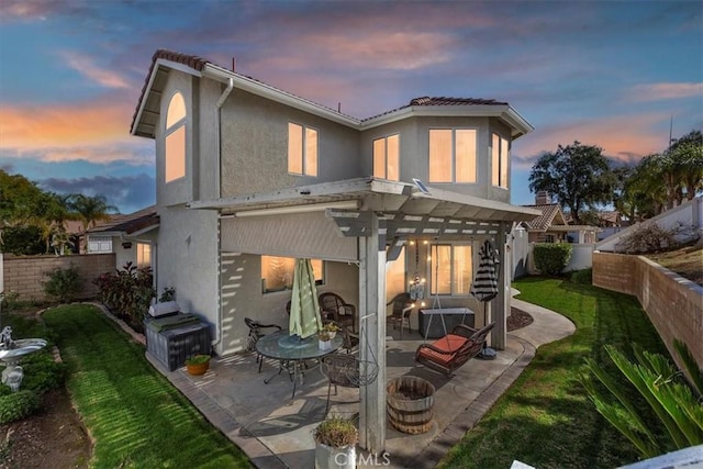 back of house at dusk featuring a patio, a fenced backyard, a yard, stucco siding, and a pergola