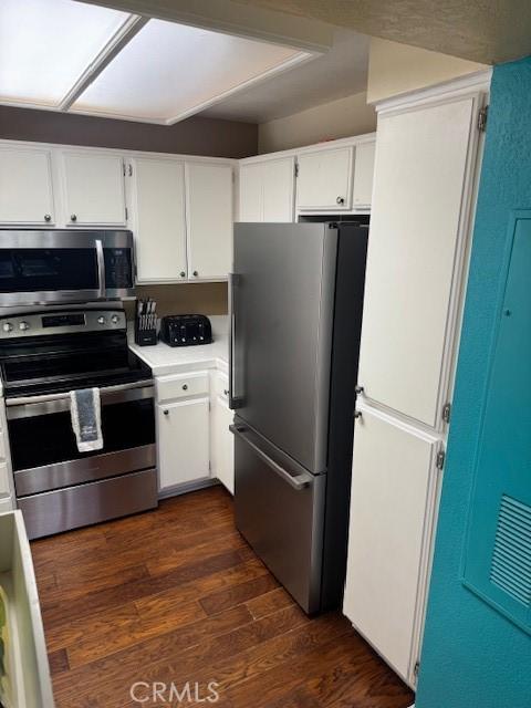 kitchen with light countertops, appliances with stainless steel finishes, dark wood finished floors, and white cabinetry