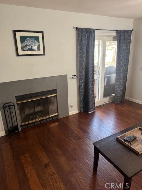 unfurnished living room with dark wood-type flooring, baseboards, and a tiled fireplace