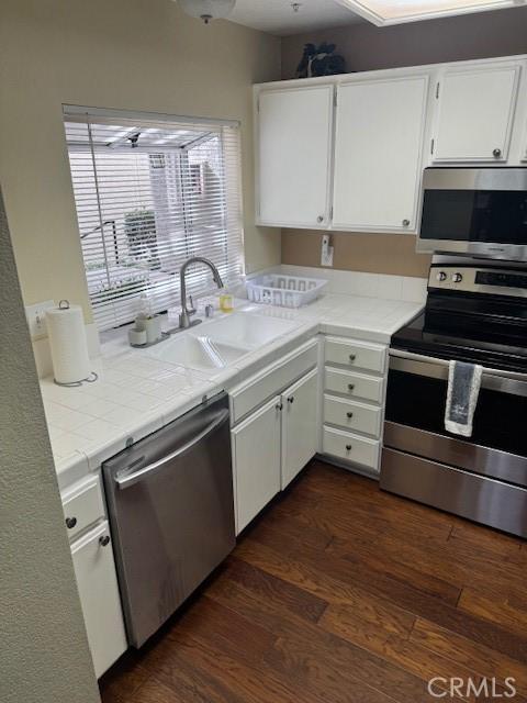 kitchen with tile countertops, dark wood-style flooring, a sink, white cabinetry, and appliances with stainless steel finishes