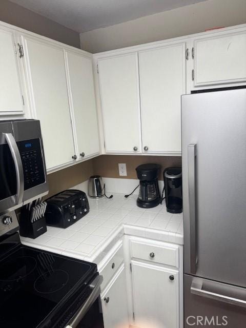 kitchen with tile counters, appliances with stainless steel finishes, and white cabinetry