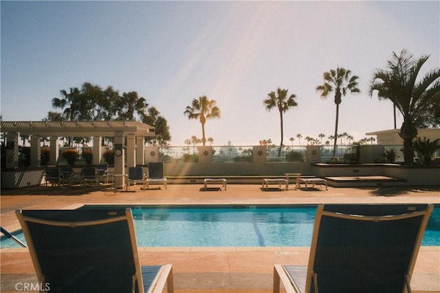 pool at dusk featuring a community pool, fence, and a pergola