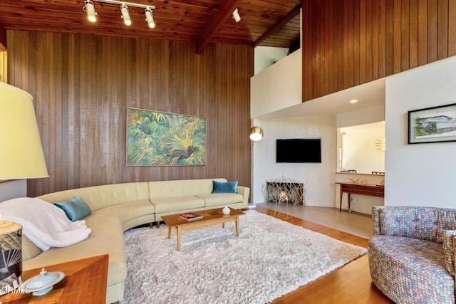 living area with beam ceiling, wood ceiling, a large fireplace, wood walls, and track lighting