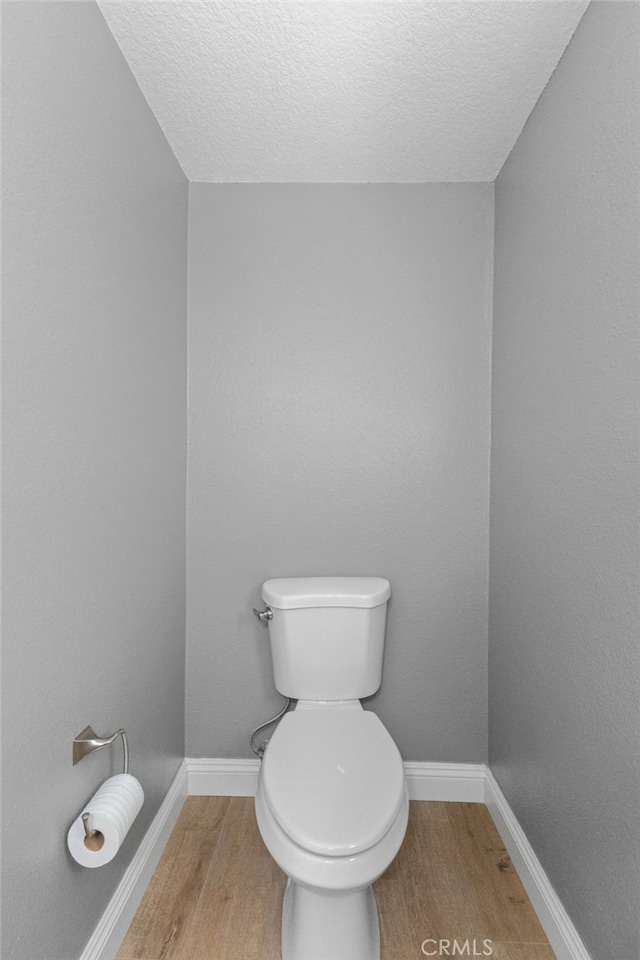 half bath with toilet, a textured ceiling, baseboards, and wood finished floors