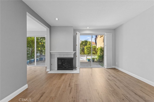 unfurnished living room featuring light wood-style floors, a fireplace with flush hearth, and a healthy amount of sunlight