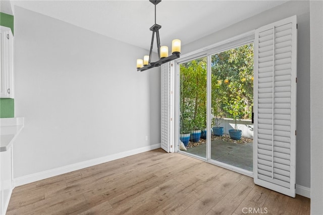 unfurnished dining area with a chandelier, baseboards, and light wood-style floors