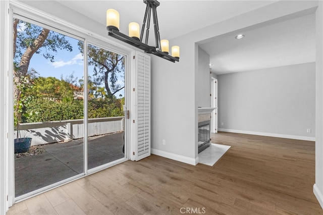 unfurnished dining area with a fireplace with flush hearth, a healthy amount of sunlight, baseboards, and wood finished floors