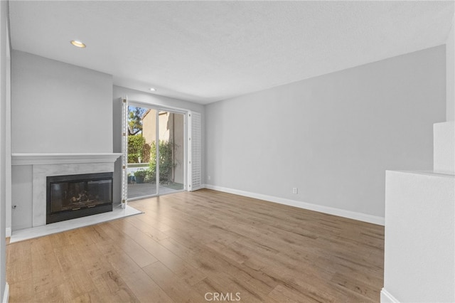 unfurnished living room featuring a textured ceiling, light wood-style flooring, recessed lighting, baseboards, and a glass covered fireplace