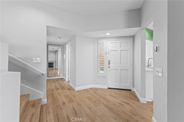 foyer featuring a fireplace, light wood-style flooring, baseboards, and stairs