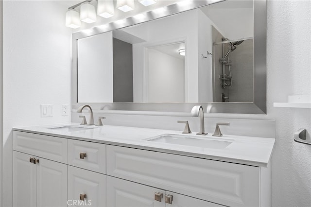 bathroom featuring a shower, a textured wall, a sink, and double vanity