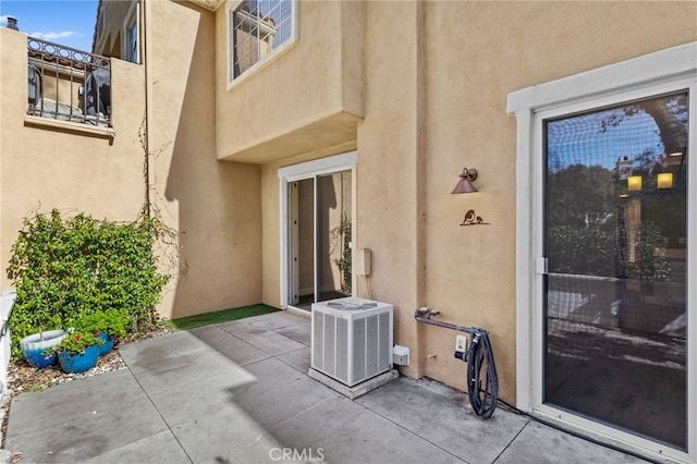 view of exterior entry featuring central air condition unit, stucco siding, and a patio