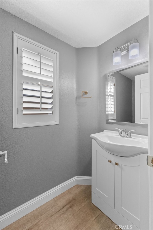 bathroom with a textured wall, vanity, baseboards, and wood finished floors