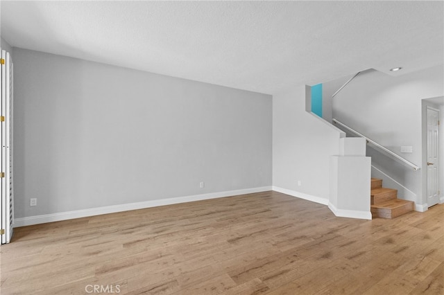 unfurnished living room featuring a textured ceiling, stairway, light wood-style flooring, and baseboards