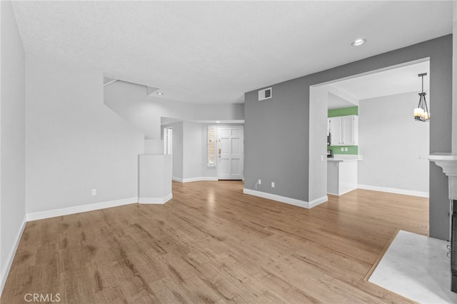 unfurnished living room featuring a fireplace with flush hearth, light wood-type flooring, visible vents, and baseboards