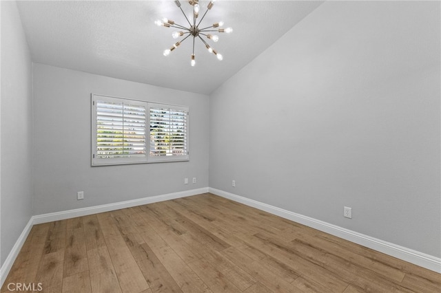 unfurnished room featuring an inviting chandelier, baseboards, vaulted ceiling, and wood finished floors