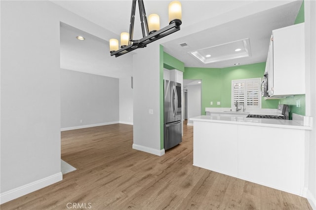 kitchen with a peninsula, white cabinets, light countertops, appliances with stainless steel finishes, and a raised ceiling