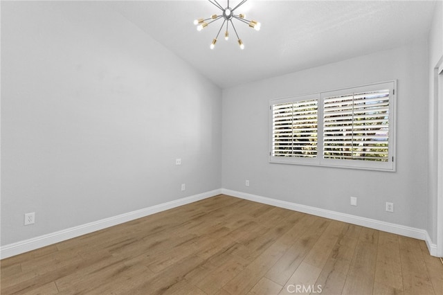 unfurnished room featuring a chandelier, wood finished floors, and baseboards