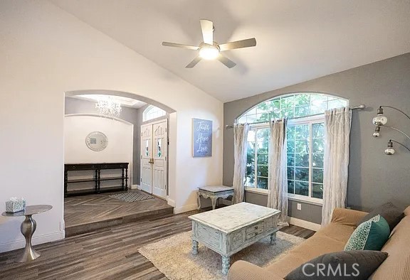 living area featuring dark wood-type flooring, lofted ceiling, ceiling fan, and baseboards