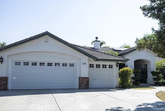 view of front of house featuring brick siding, a chimney, stucco siding, concrete driveway, and an attached garage