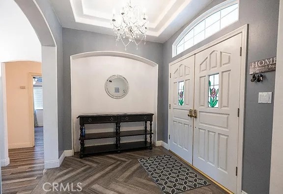 entryway with a notable chandelier, a tray ceiling, arched walkways, and baseboards