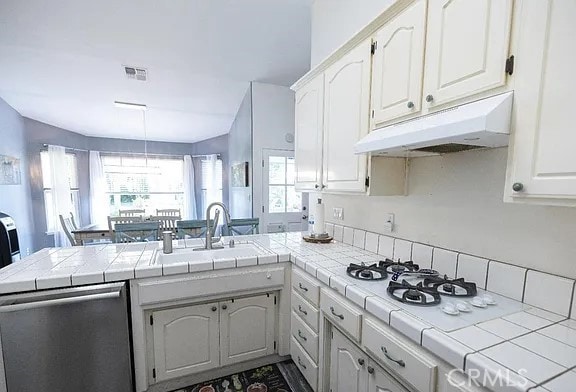 kitchen featuring under cabinet range hood, dishwasher, tile countertops, and a peninsula