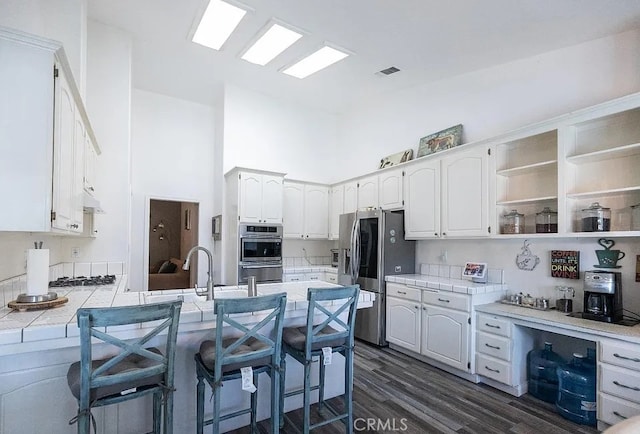 kitchen with a peninsula, a breakfast bar, white cabinets, appliances with stainless steel finishes, and open shelves