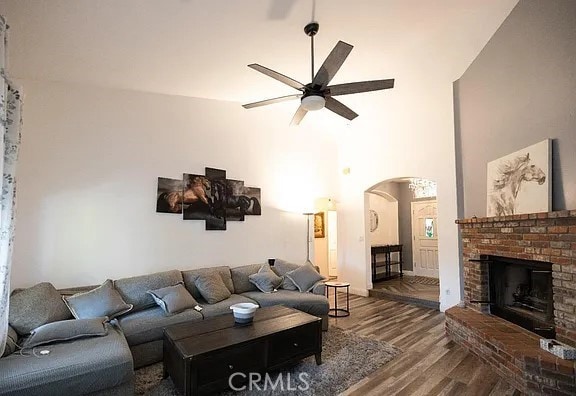 living room with ceiling fan, arched walkways, a brick fireplace, and wood finished floors