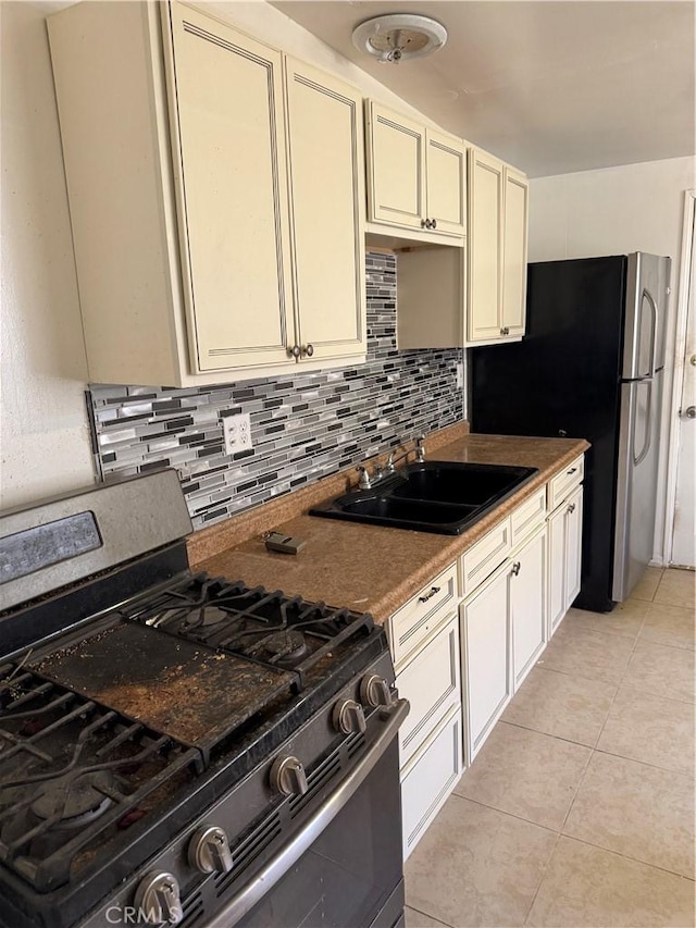 kitchen featuring cream cabinetry, light tile patterned floors, stainless steel appliances, tasteful backsplash, and a sink