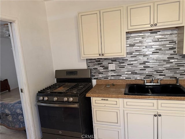 kitchen with a sink, cream cabinetry, dark countertops, and stainless steel range with gas cooktop