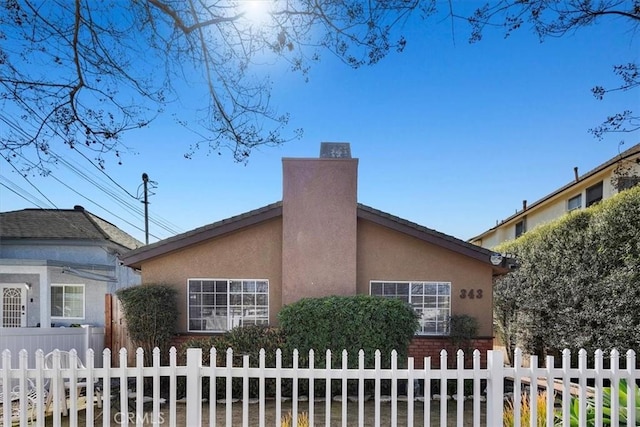 view of home's exterior with a fenced front yard, a chimney, and stucco siding