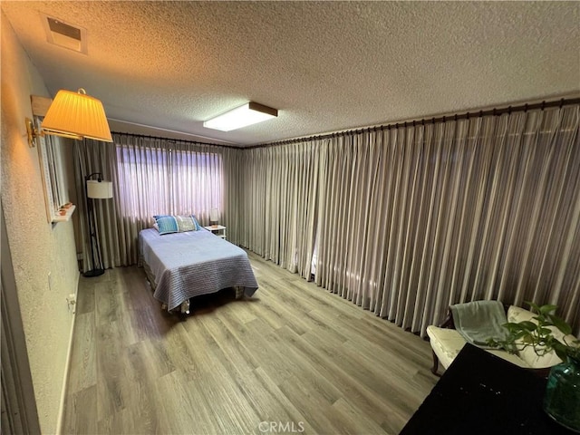 bedroom with a textured ceiling, a textured wall, light wood-type flooring, and visible vents