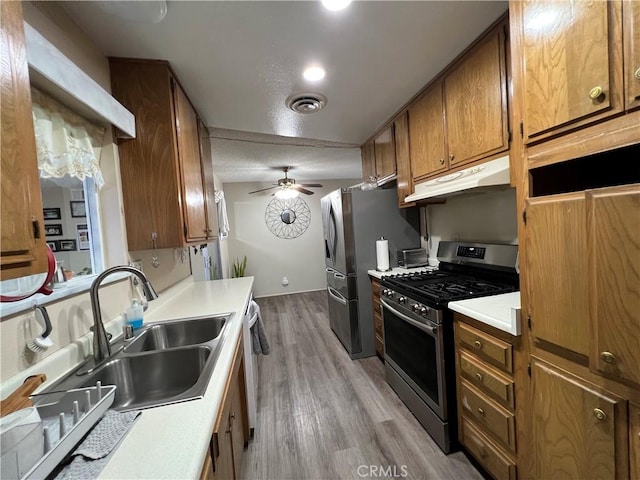 kitchen featuring brown cabinets, stainless steel appliances, visible vents, a sink, and under cabinet range hood