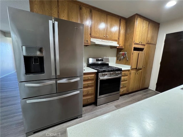 kitchen featuring under cabinet range hood, stainless steel appliances, light countertops, and brown cabinetry