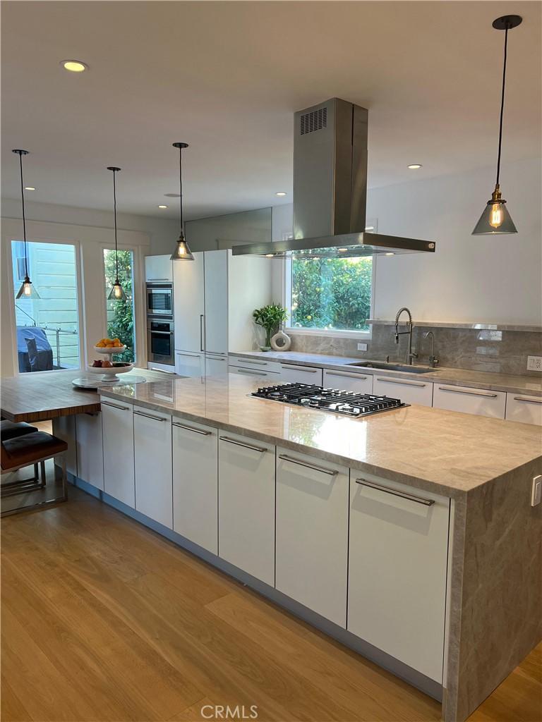 kitchen featuring island range hood, white cabinets, stainless steel appliances, light wood-type flooring, and a sink