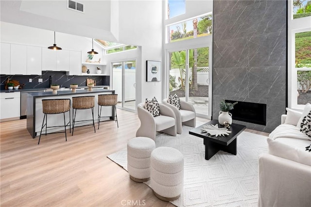 living area featuring a high ceiling, light wood-type flooring, a high end fireplace, and visible vents