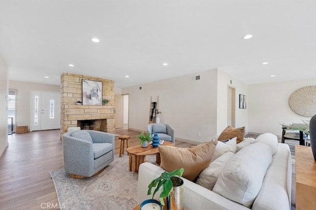 living room featuring light wood-style flooring, recessed lighting, a fireplace, visible vents, and baseboards