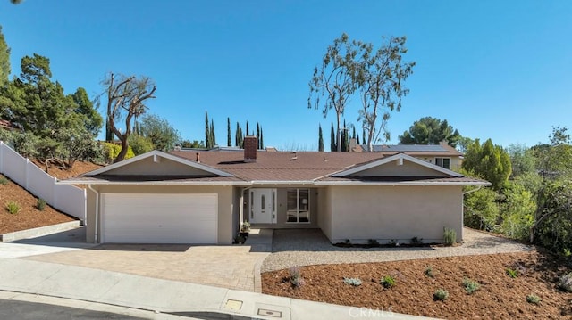 ranch-style house featuring a garage, driveway, a chimney, fence, and stucco siding