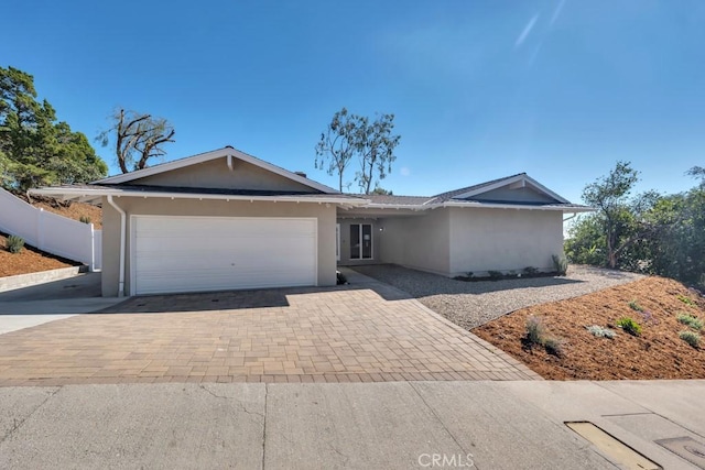 ranch-style house with a garage, decorative driveway, fence, and stucco siding