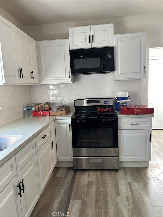 kitchen featuring black microwave, wood finished floors, light countertops, white cabinetry, and gas stove