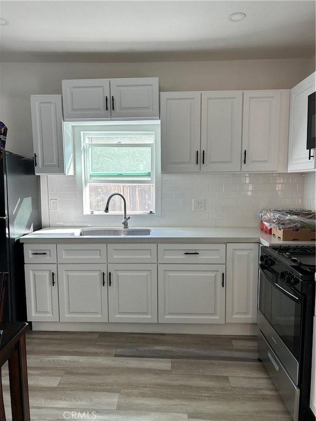 kitchen with a sink, white cabinetry, light countertops, freestanding refrigerator, and range with gas cooktop