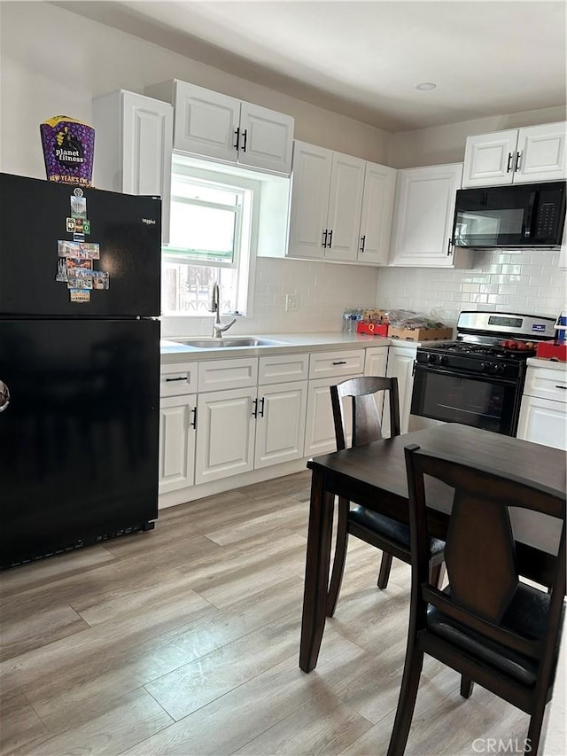 kitchen featuring light wood-style floors, light countertops, black appliances, white cabinetry, and a sink