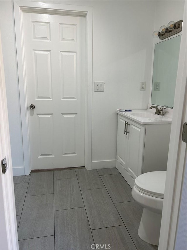 half bathroom featuring baseboards, vanity, and toilet