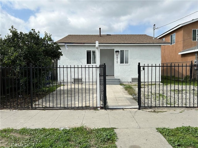 bungalow-style house featuring roof with shingles, a fenced front yard, a gate, and stucco siding