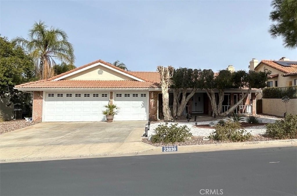 view of front of house with a garage, covered porch, concrete driveway, and a tiled roof