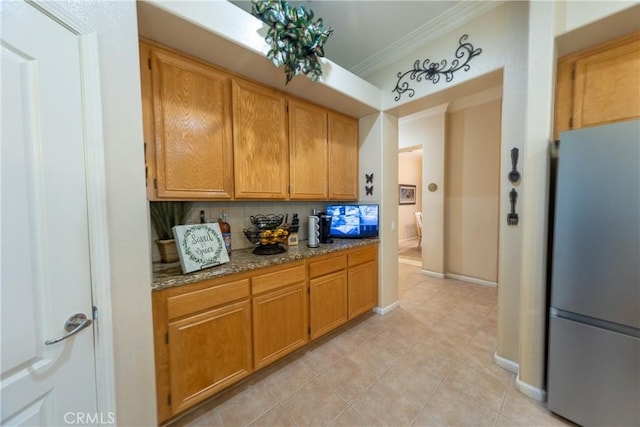 kitchen with light stone counters, baseboards, freestanding refrigerator, decorative backsplash, and crown molding