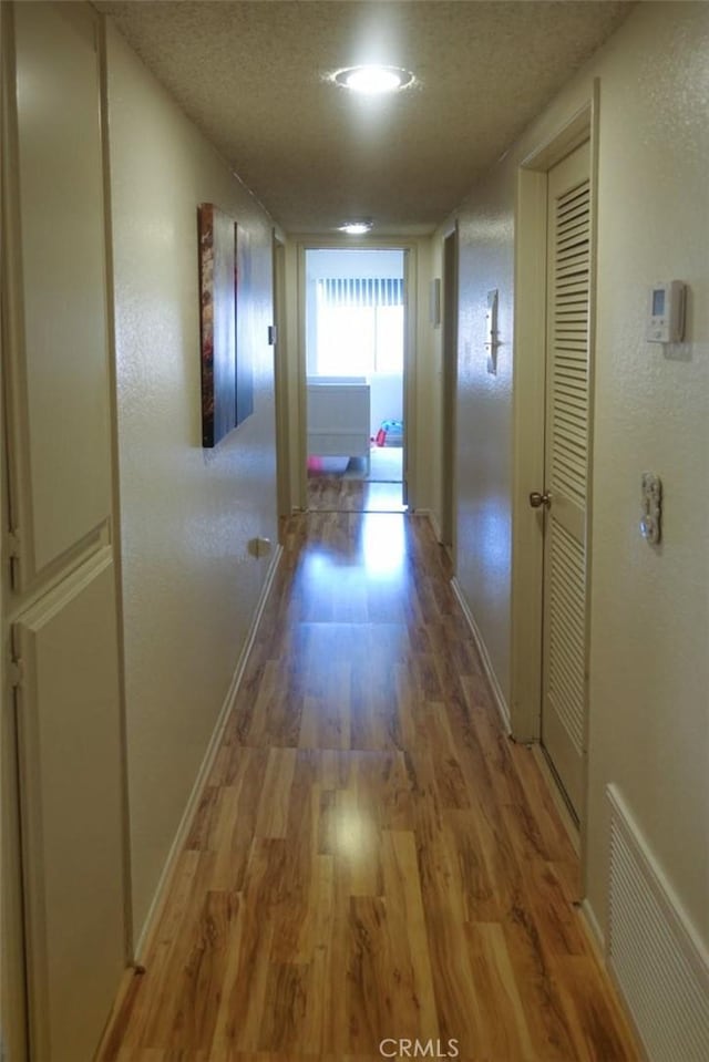 corridor featuring a textured ceiling, wood finished floors, visible vents, and baseboards