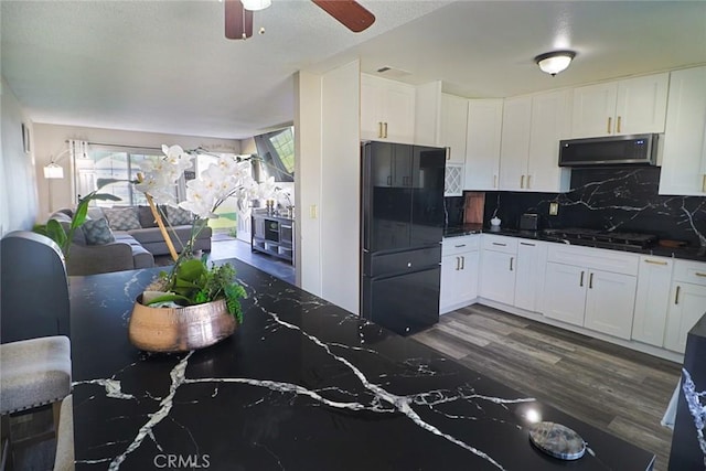 kitchen featuring dark wood-type flooring, stainless steel microwave, dark countertops, gas stovetop, and freestanding refrigerator