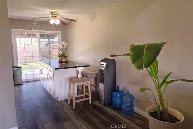 kitchen with dark wood-type flooring, a kitchen breakfast bar, a textured ceiling, a center island, and white cabinets