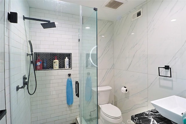 bathroom featuring visible vents, a shower stall, toilet, tile walls, and a sink