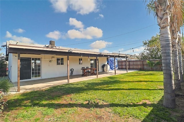 rear view of house featuring a patio, a yard, fence, and stucco siding